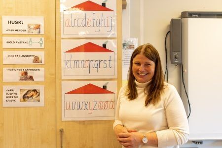 Astrid Knutson ved siden av smittevernregler hengt opp i klasserommet. Foto: Håvard Storsæter.
