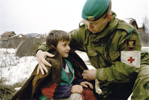 KOSOVOKRIGEN I 1999: En norsk sanitetssoldat fra Telemarkbataljonen hjelper en kosovoalbansk gutt å holde varmen. FOTO: Torbjørn Kjosvold / Forsvarets mediesenter